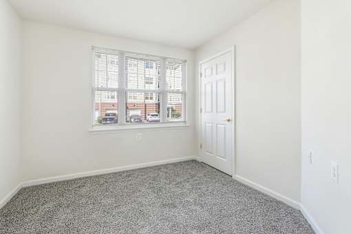 A room with a carpeted floor, a window with blinds, and a door.