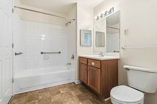 A white tiled bathroom with a wooden vanity and a white toilet.