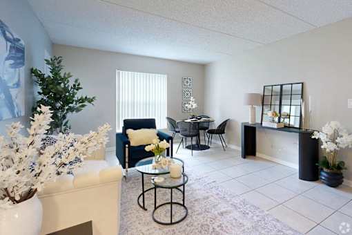 A living room with a white couch, a black chair, a coffee table, and a plant.