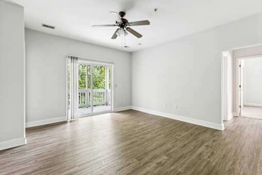 A room with a ceiling fan and sliding glass doors leading to a balcony.
