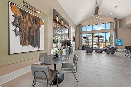 A modern dining room with a large abstract painting on the wall and a view of the outdoors through the windows.