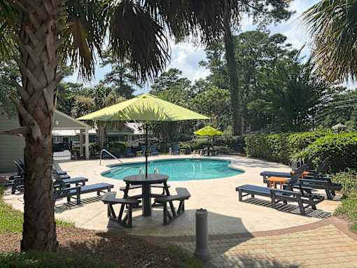 A pool surrounded by trees and a picnic table.
