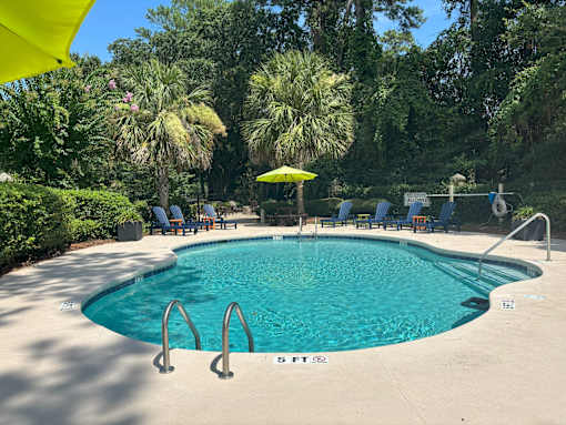 A swimming pool surrounded by trees and chairs.