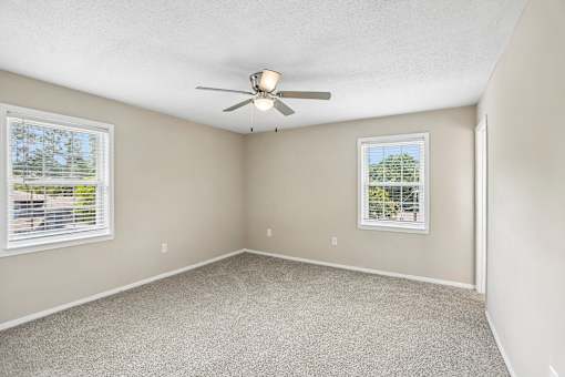 A room with a ceiling fan and two windows.