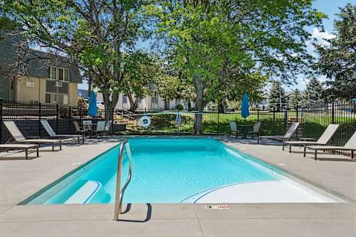 A swimming pool surrounded by trees and lounge chairs.