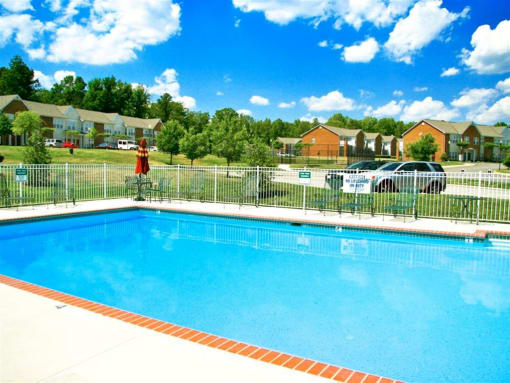 a swimming pool with a fence and houses in the background at Chester Village Green Apartments, Chester, Virginia