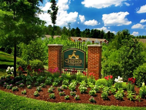 a sign in front of a garden with a building in the background at Chester Village Green Apartments, Chester, VA