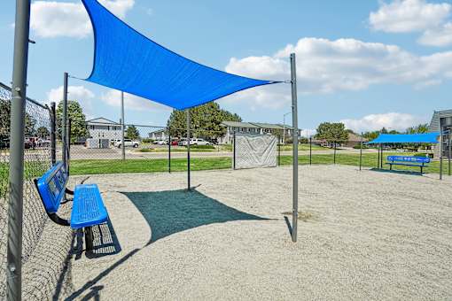 A blue shade structure is in a sandy area with benches.