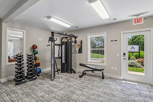 A gym room with a bench, weights, and a window.