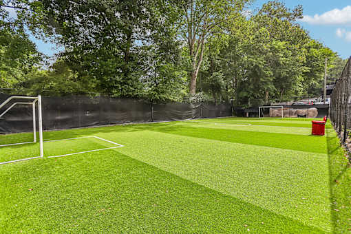 A soccer field with a green surface and a red bin.