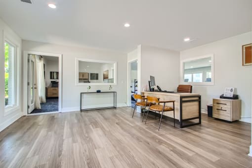 a living room with a desk and chairs and a kitchen