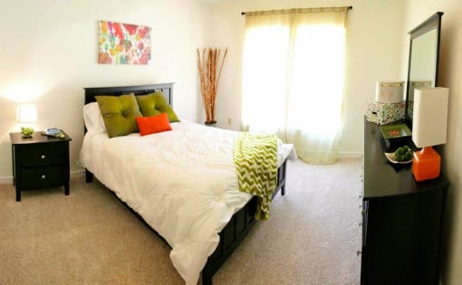 a bedroom with a white bed and green and orange pillows at Chester Village Green Apartments, Chester, Virginia