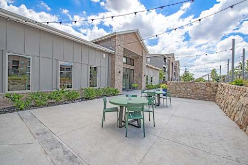 A patio with a table and chairs is surrounded by a stone wall and buildings.
