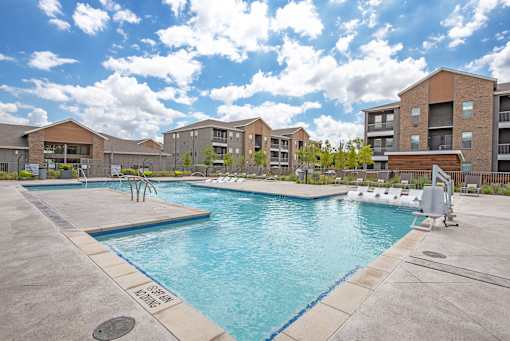 A swimming pool surrounded by a concrete floor and buildings in the background.