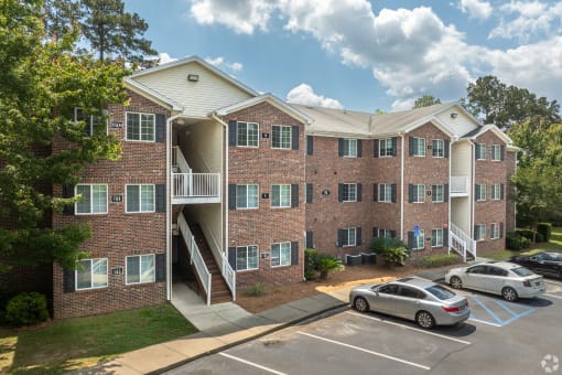 a brick apartment building with stairs and cars parked in a parking lot