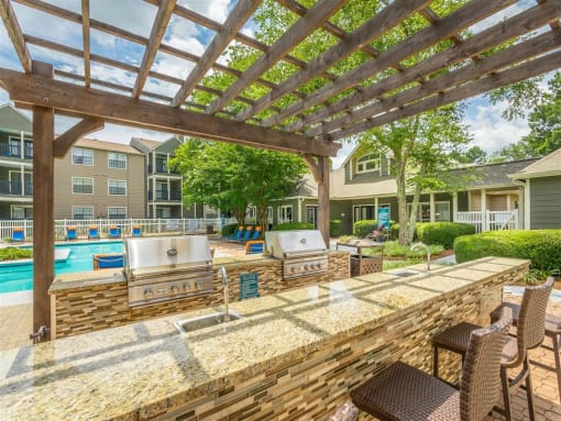 a poolside outdoor kitchen featuring 2 grills and a counter at Avenues of Kennesaw East & West, Kennesaw, GA 30144