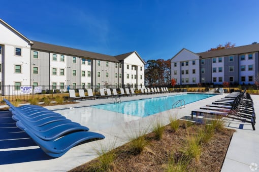 a swimming pool with chaise lounge chairs in front of an apartment building