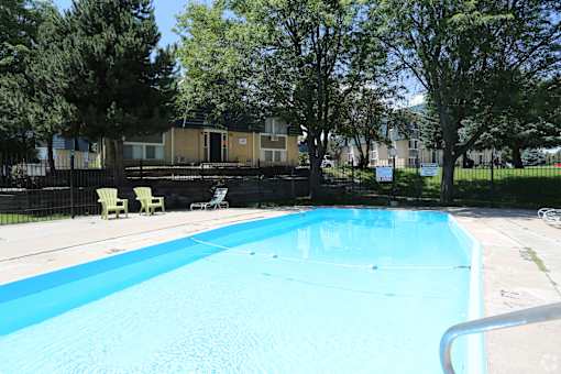 A swimming pool surrounded by trees and chairs.