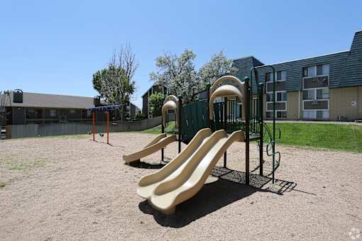 A playground with a yellow slide and a green fence.