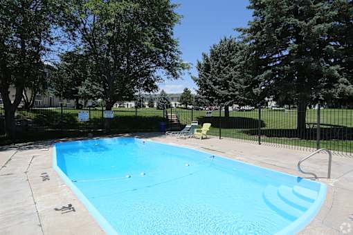A blue swimming pool surrounded by a black fence and trees.