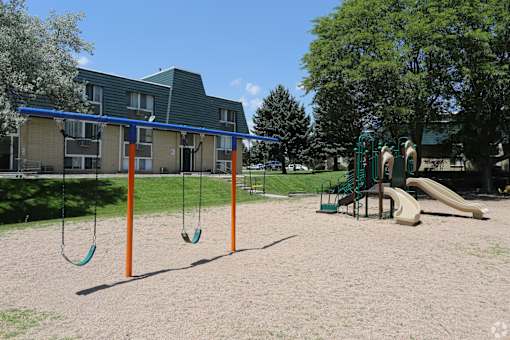 A playground with swings and a slide in front of a building.