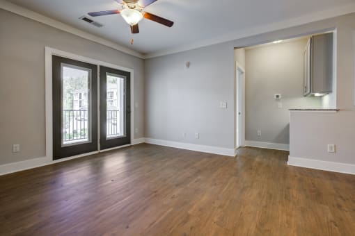 an empty living room with a ceiling fan and french doors to a balcony