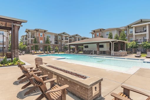 a swimming pool with chairs and a fire pit in front of an apartment building