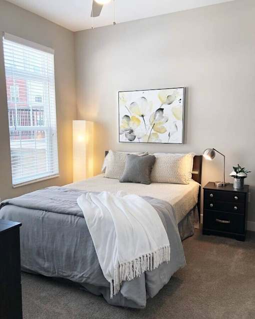 A bedroom with a bed, nightstand, and a painting on the wall.
