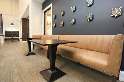 A black table with a tan couch in front of a black wall with clocks on it.