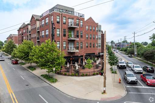A street view of a red brick building with cars parked on the side of the road.