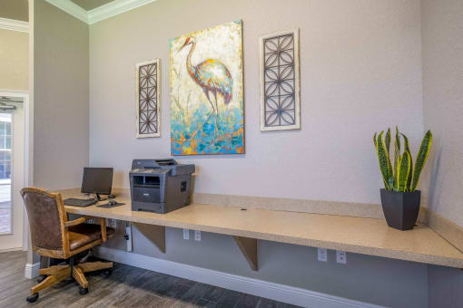 a desk with a computer and a painting on the wall
