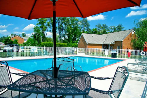 a swimming pool with a table and chairs under an umbrella at Chester Village Green Apartments, Virginia, 23831