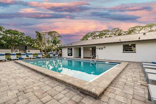 A swimming pool surrounded by a brick patio and a white building.