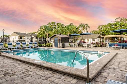 A swimming pool surrounded by a stone patio and lounge chairs.