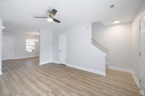 A room with a ceiling fan and light fixture, wooden flooring, and white walls.
