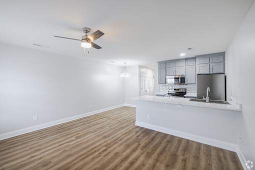 A spacious room with a ceiling fan and a kitchenette in the corner.