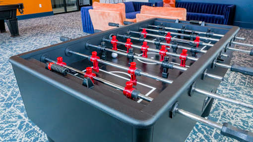 A foosball table with red and black players is in the foreground.