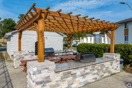 a wooden pergola with a stone wall around it and a stone grill with a grill at Summit Augusta, Augusta, GA