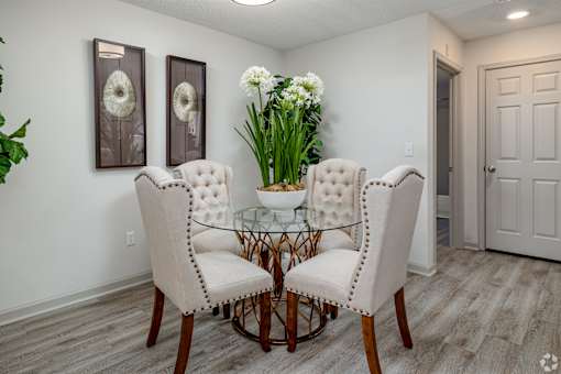 A dining room with a glass table and white chairs.