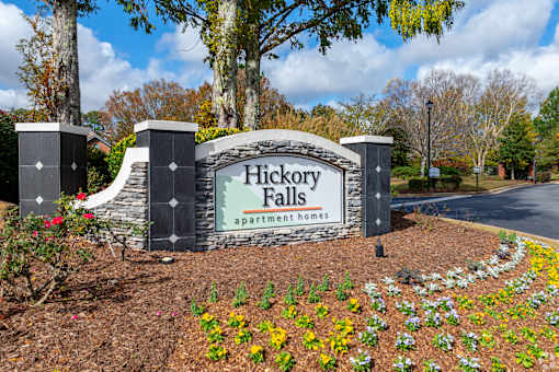 A sign for Hickory Falls Apartment Homes is surrounded by flowers and trees.