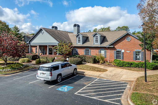A silver minivan is parked in a handicapped spot in front of a brick building.