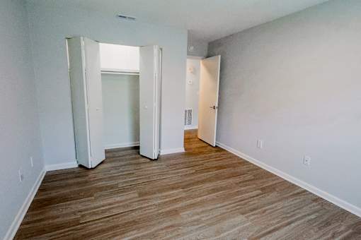 A room with wooden floors and white walls with a doorway open to another room.