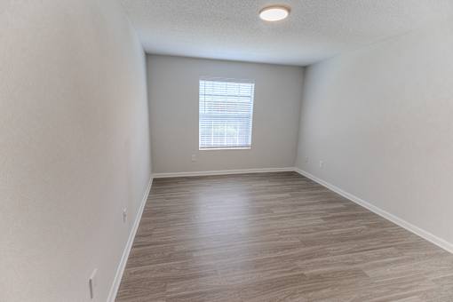 A room with wooden flooring and a window with blinds.
