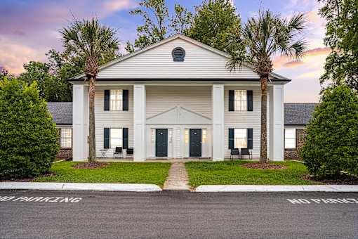 A white building with a black door and windows is surrounded by greenery.