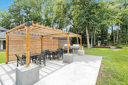 A wooden pergola with a table and chairs is set up in a backyard.