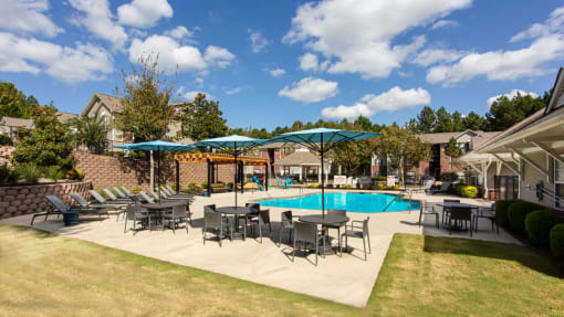 a swimming pool with tables and umbrellas in front of a house
