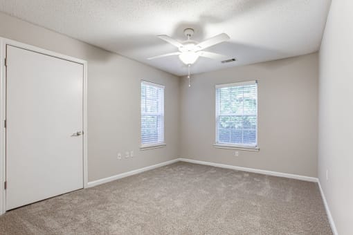 an empty room with a ceiling fan and two windows