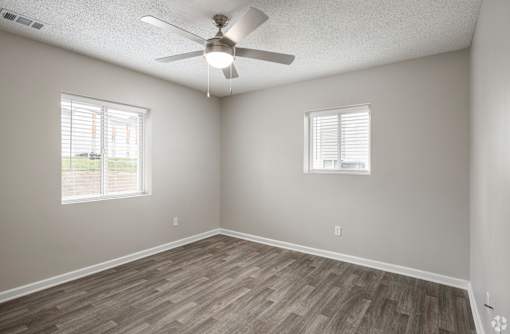 A room with a ceiling fan and two windows.
