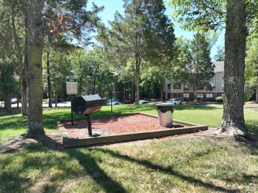 a park with a grill and trees and a building
