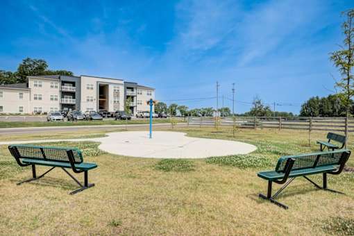 A park with two benches and a playground in front of apartment buildings.